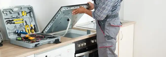 Cooktop repair technician lifting a built-in stovetop for service in Bloomington, IN