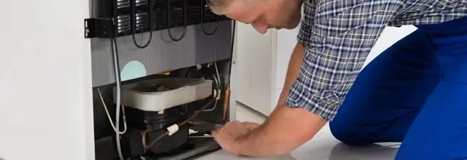 Refrigerator repair technician servicing the compressor and condenser area in Bloomington, IN