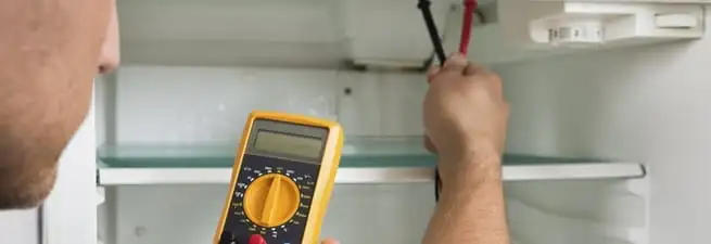 Refrigerator repair technician testing electrical components with a multimeter in Bloomington, IN