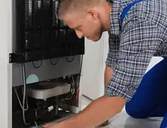 Refrigerator repair technician servicing the compressor and condenser area in Bloomington, IN