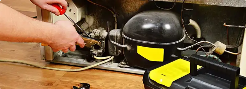 Refrigerator repair technician fixing the compressor and wiring in Bloomington, IN